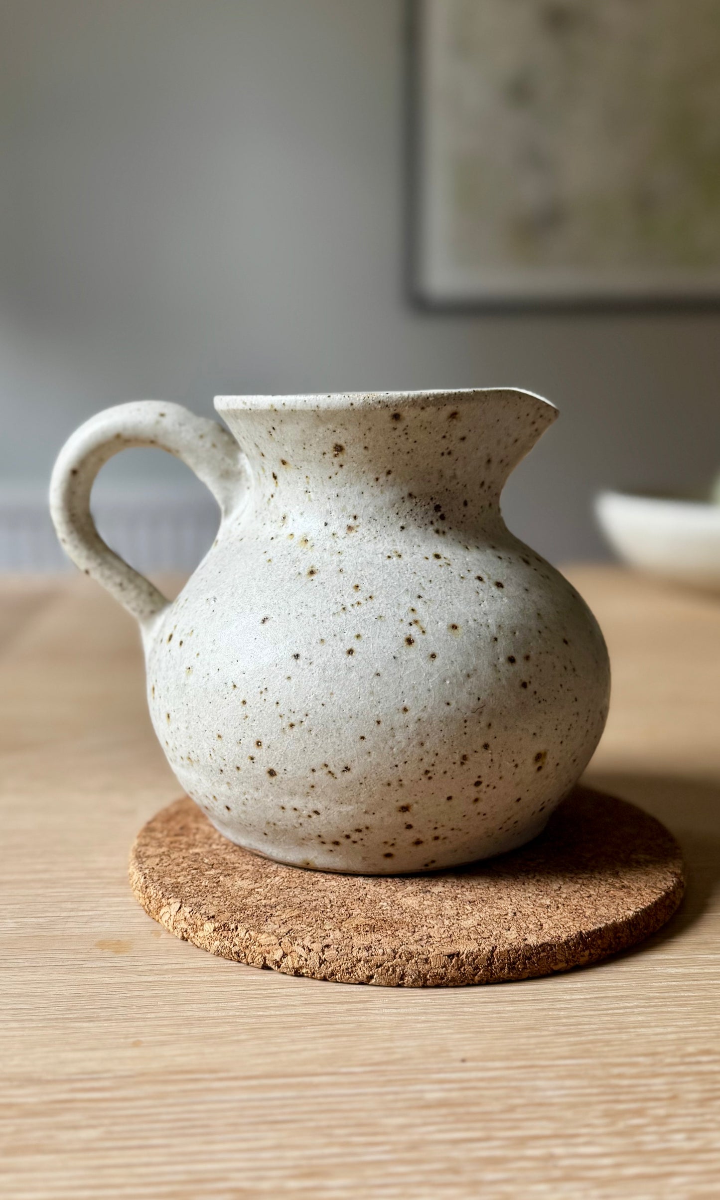 Speckled ceramic pitcher on a cork coaster with a blurred background