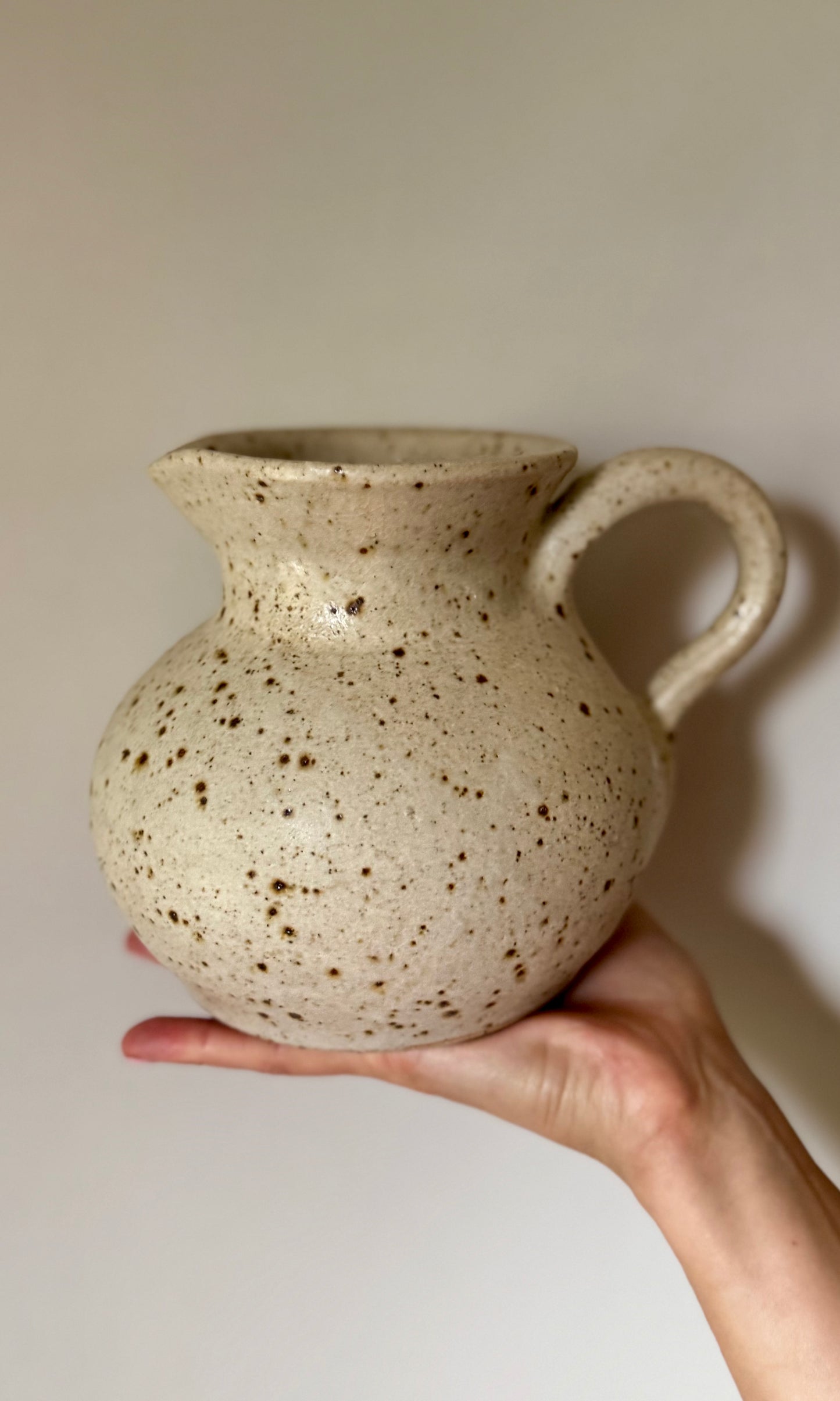 Hand holding a speckled ceramic pitcher against a plain background