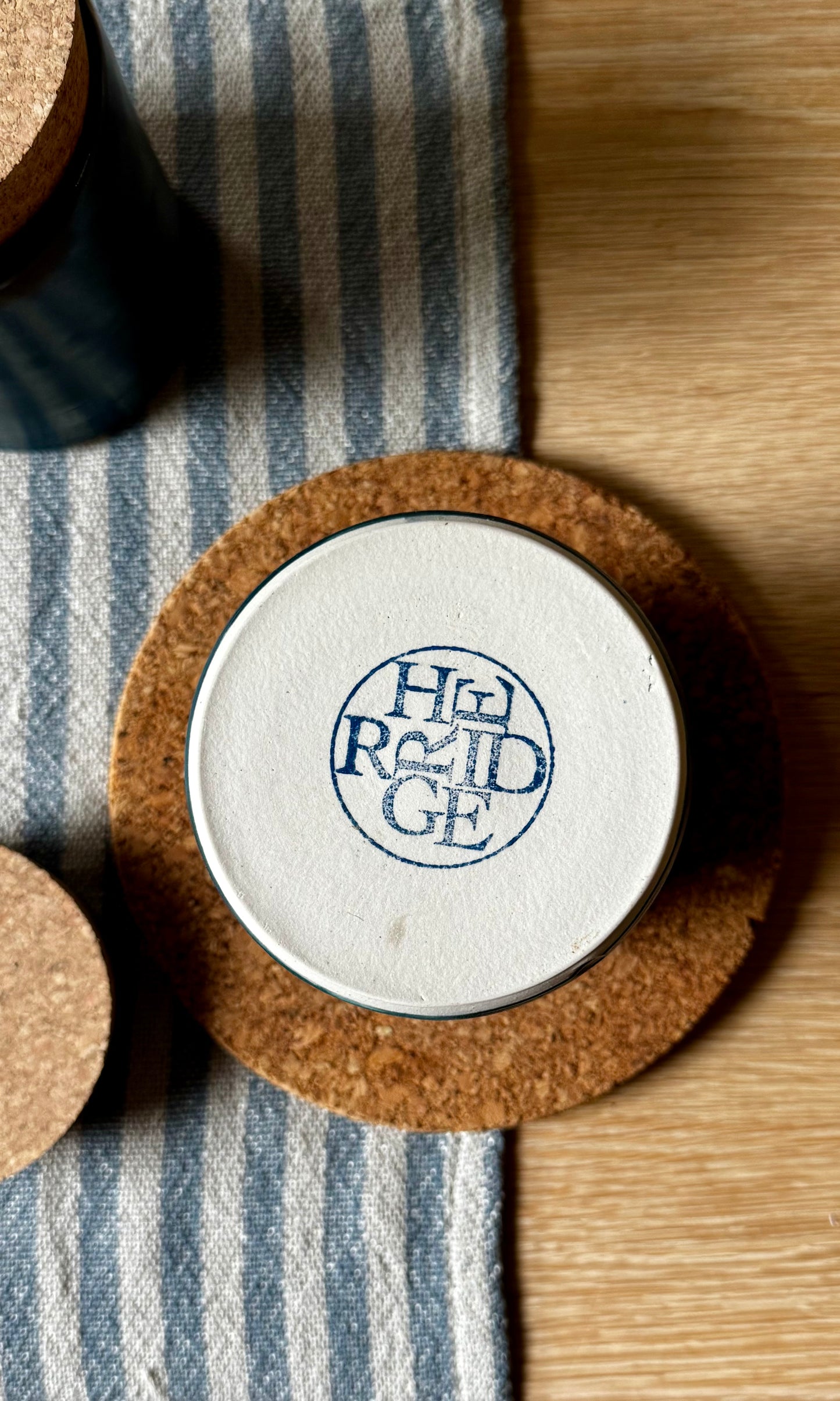 Bottom of blue ceramic container showing 'Herridge' branding on a striped fabric background.