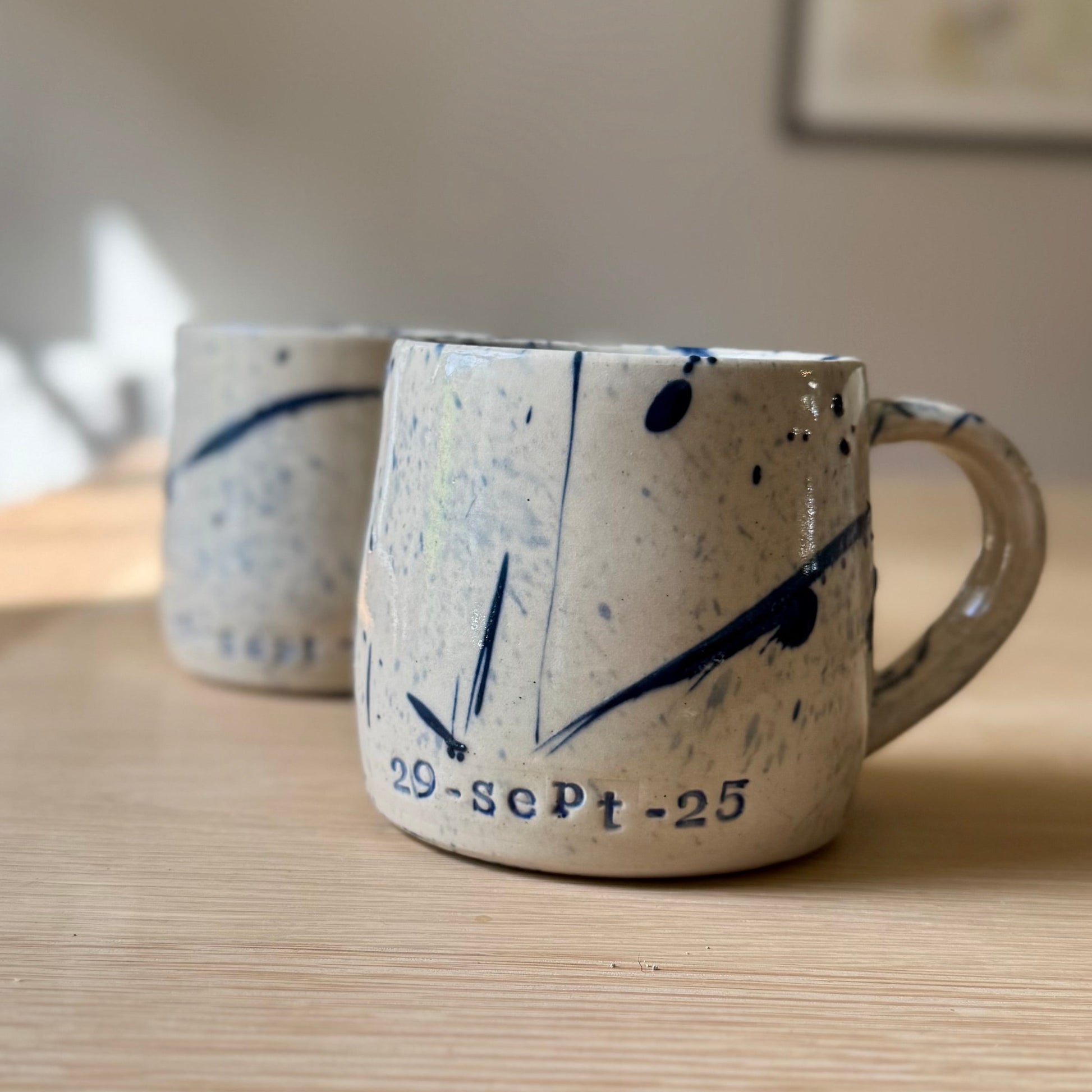Two ceramic mugs with abstract designs on a wooden surface.