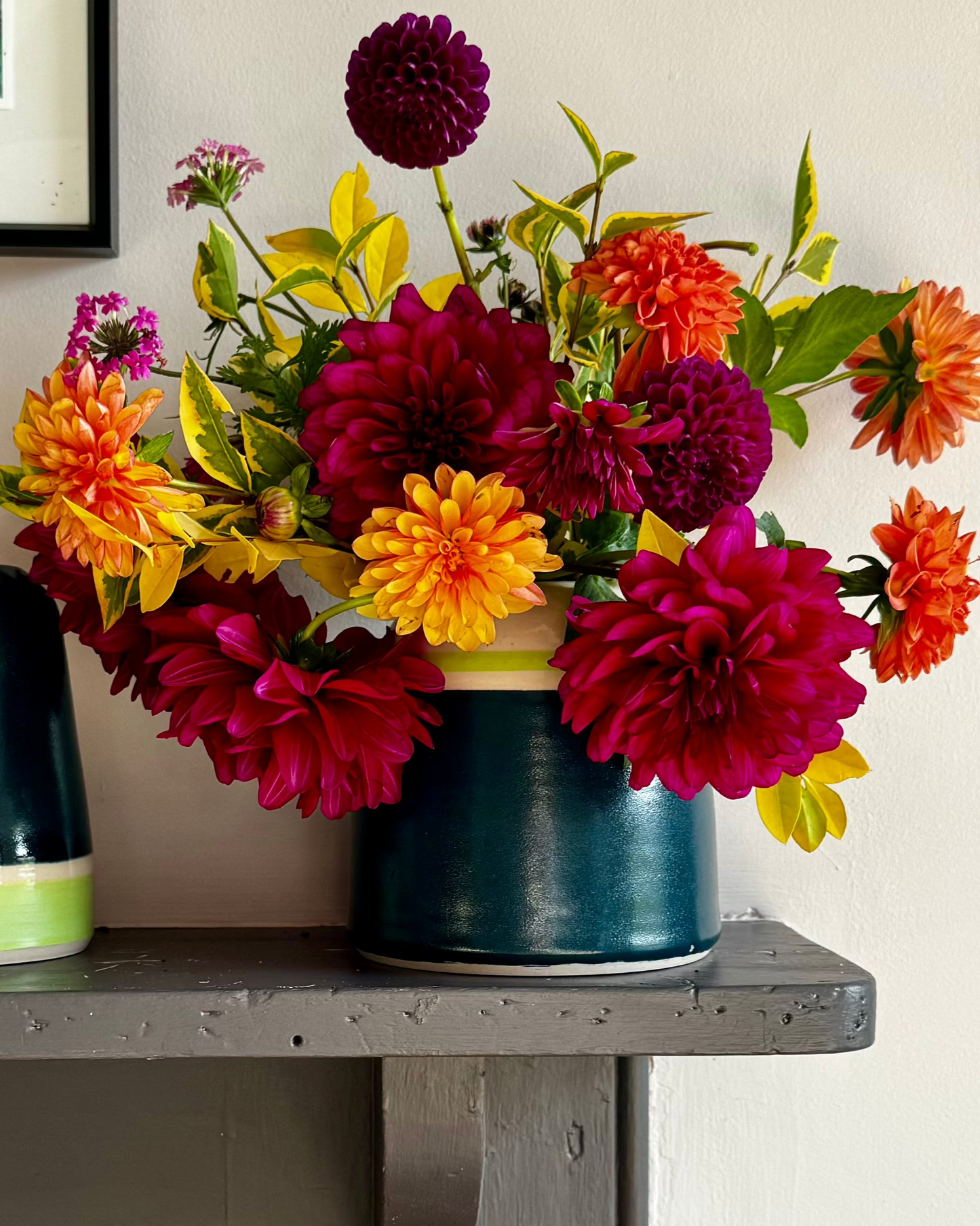 Handmade ceramic vase from Herridge Pottery in Bali Blue with lime banding. Vase contains bunch of richly coloured dahlias. Toe the side a second vase is partially shown, it is the same colour way bu the banding is inverted. 