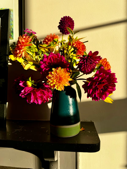 Handmade ceramic vase by Herridge Pottery on shelf. The vase is Bali blue with a lime band at the bottom. The vase contain a bunch of dahlias. 