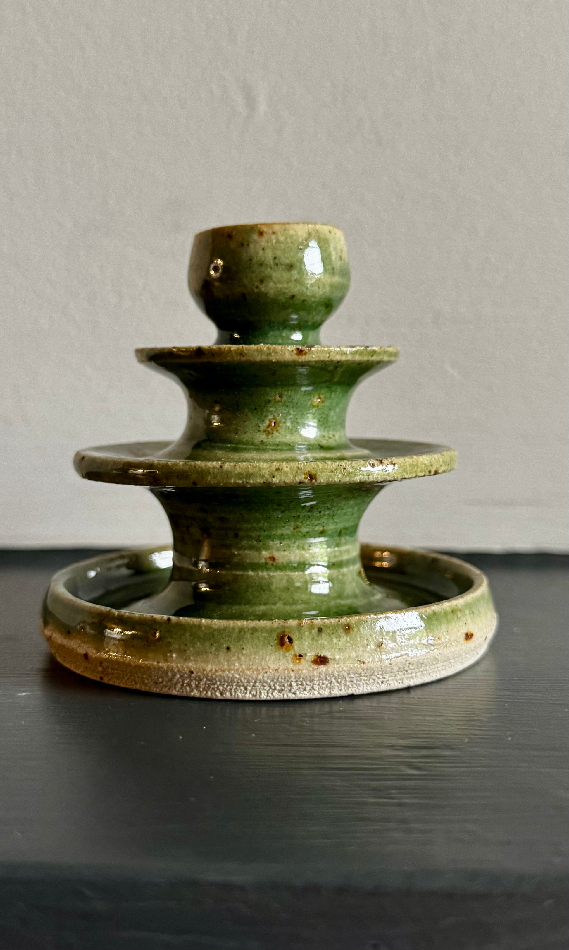 Bottle green ceramic candle holder on a dark surface with a neutral background