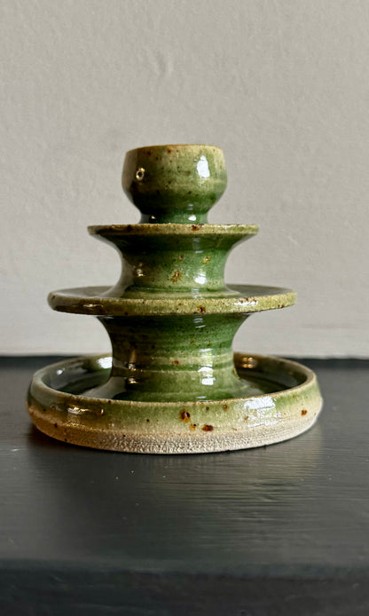 Bottle green ceramic candle holder on a dark surface with a neutral background