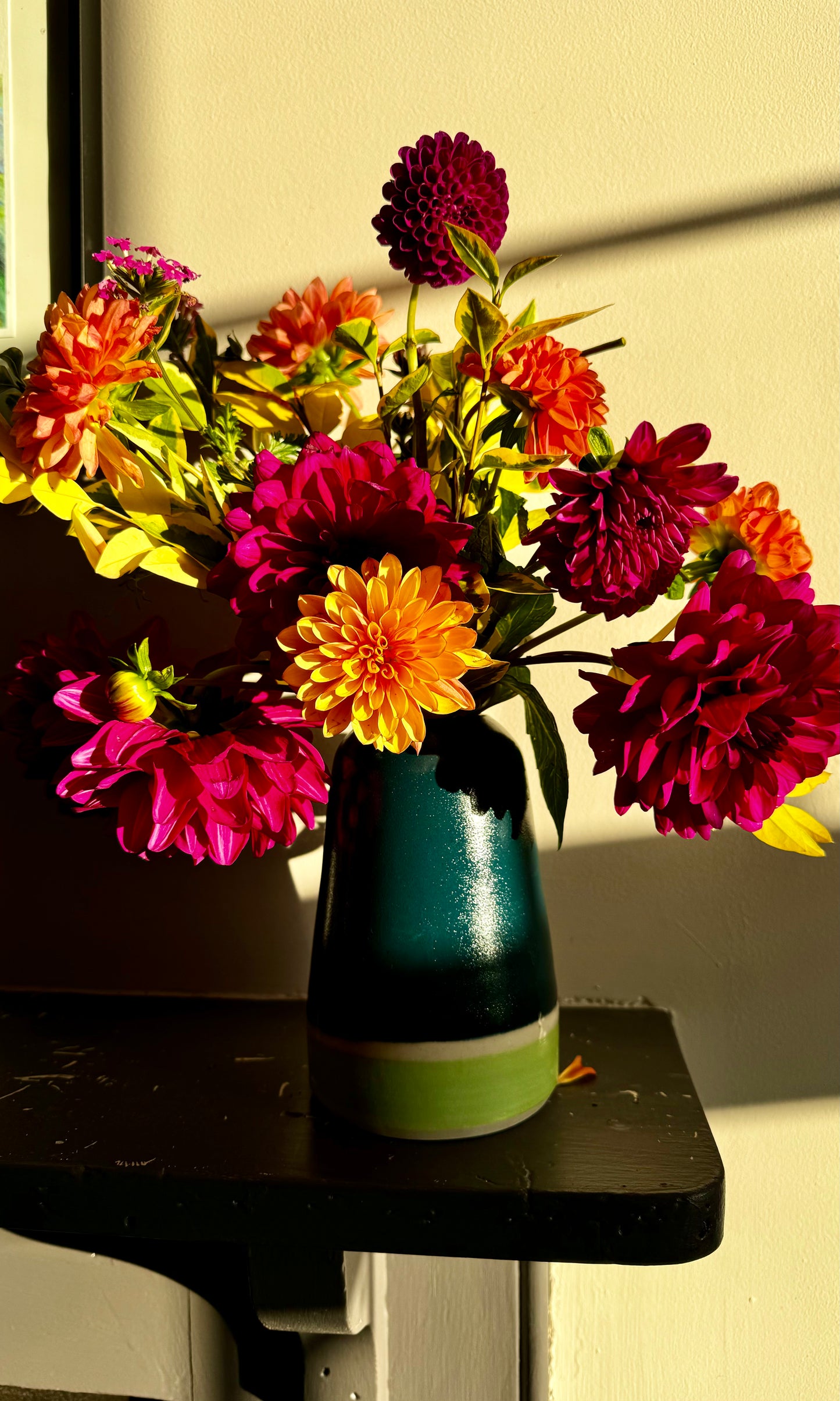 Handmade ceramic vase by Herridge Pottery on shelf. The vase is Bali blue with a lime band at the bottom. The vase contain a bunch of dahlias. 