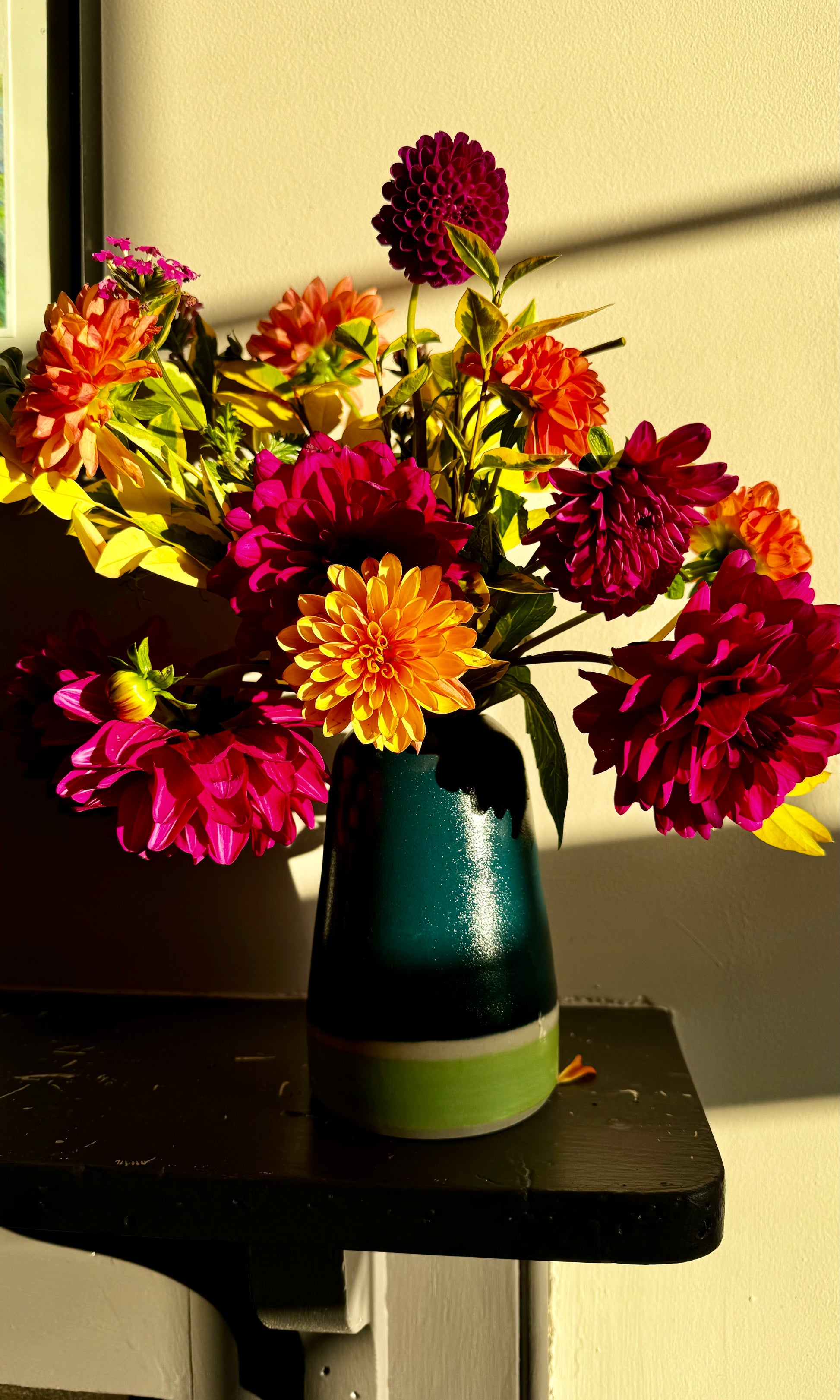 Handmade ceramic vase by Herridge Pottery on shelf. The vase is Bali blue with a lime band at the bottom. The vase contain a bunch of dahlias. 