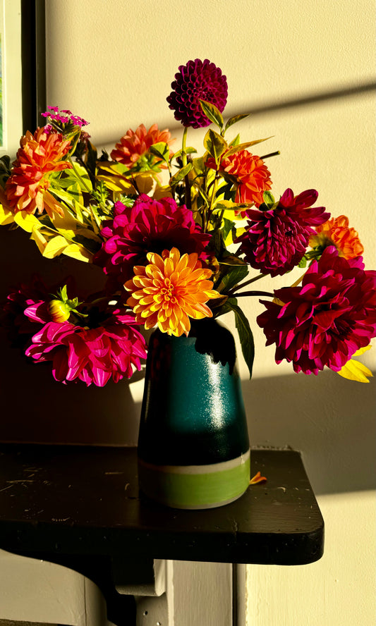 Handmade ceramic vase by Herridge Pottery on shelf. The vase is Bali blue with a lime band at the bottom. The vase contain a bunch of dahlias. 