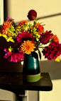 Handmade ceramic vase by Herridge Pottery on shelf. The vase is Bali blue with a lime band at the bottom. The vase contain a bunch of dahlias. 