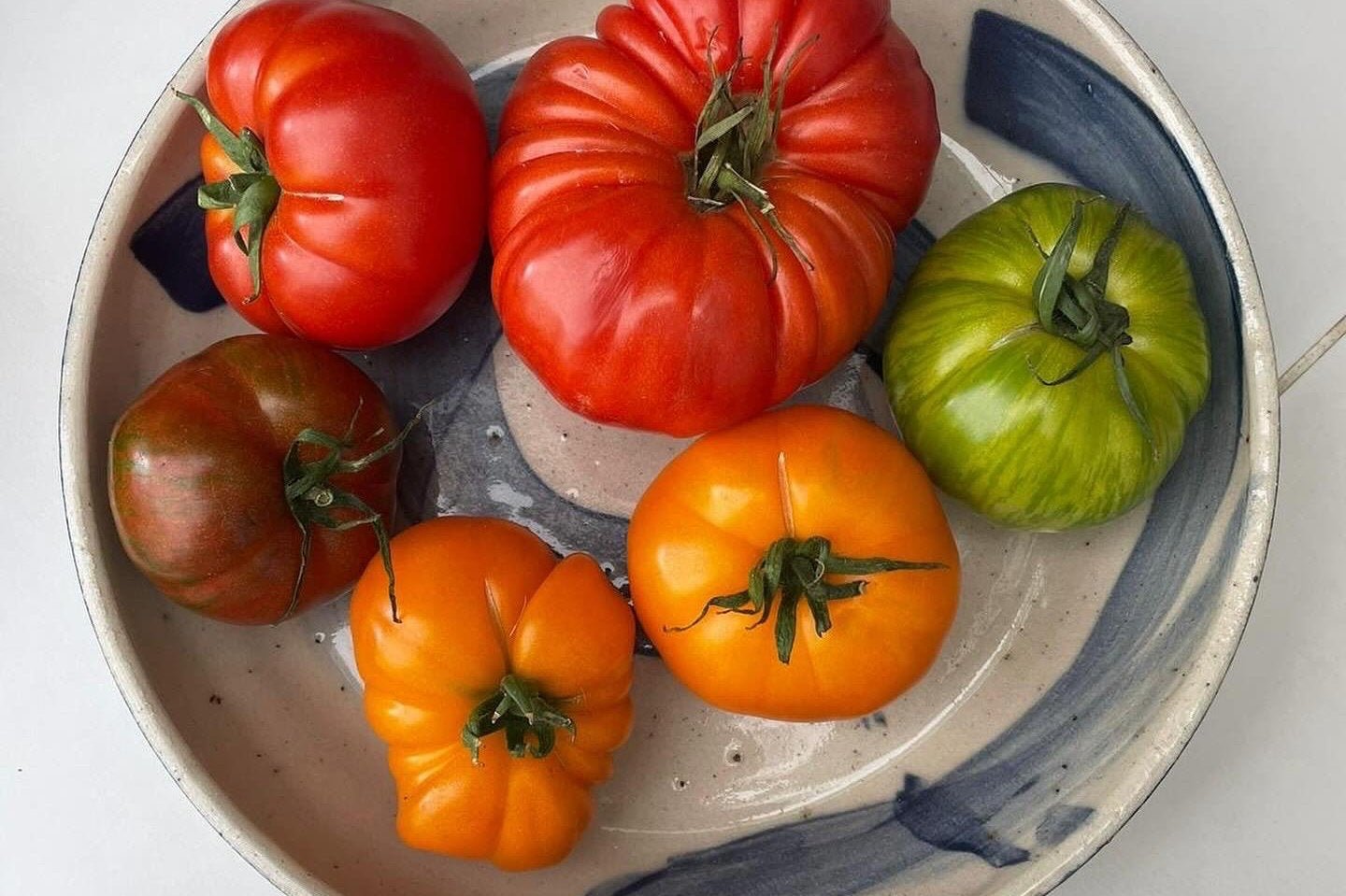 HERRIDGE POTTERY HANDMADE BLUE SWOOSH BOWL CONTAINING SELECTION OF HERITAGE TOMATOES