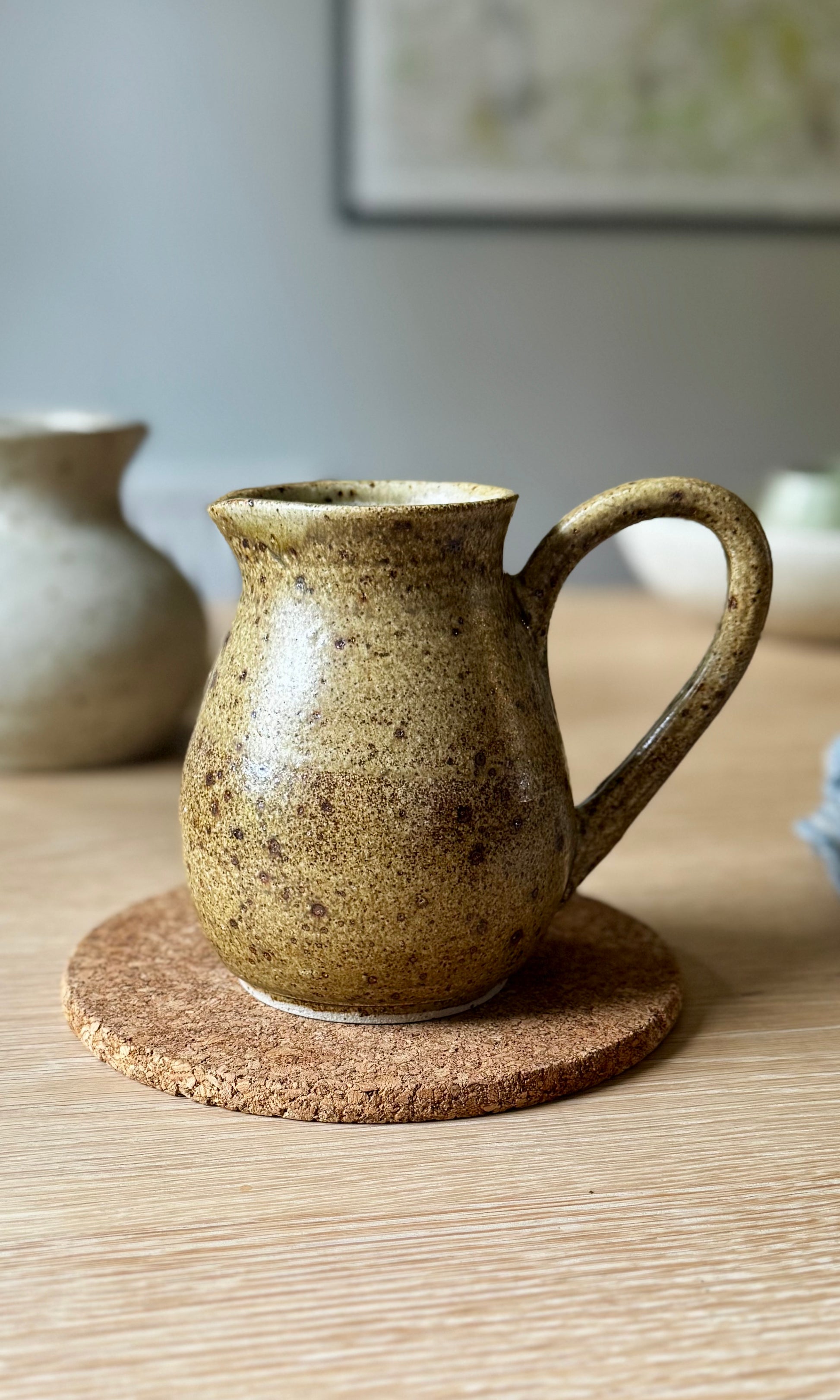 Brown ceramic pitcher on a cork coaster with a blurred background