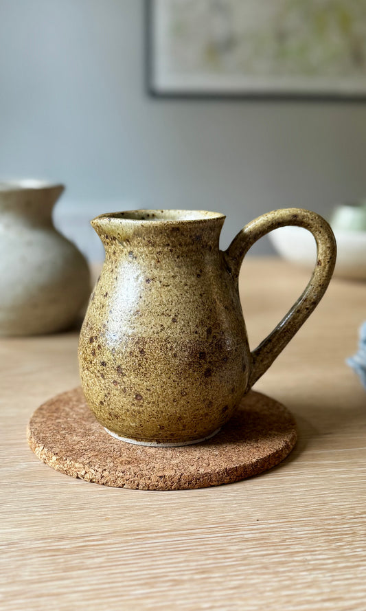 Brown ceramic pitcher on a cork coaster with a blurred background