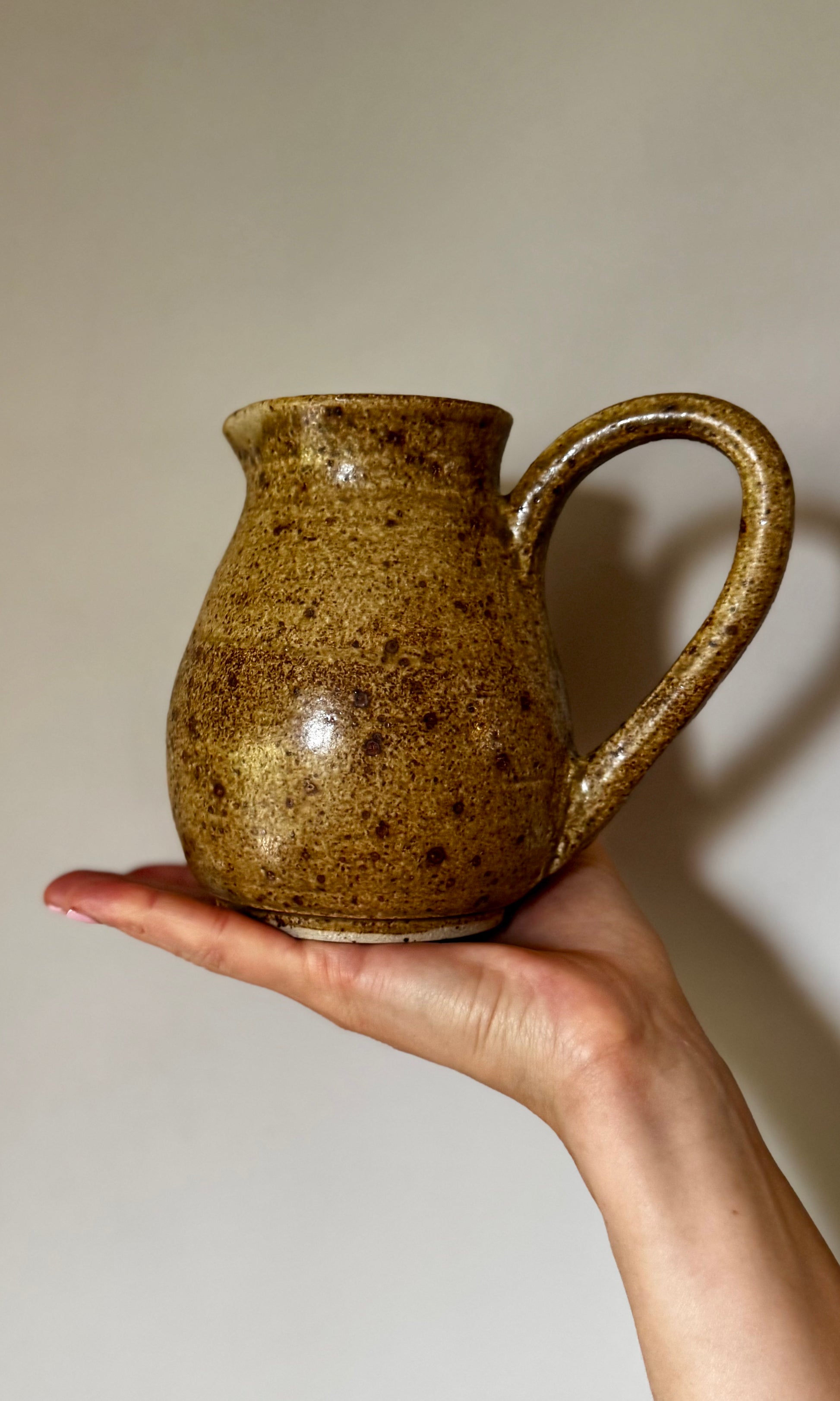 Hand holding a brown ceramic pitcher against a plain background