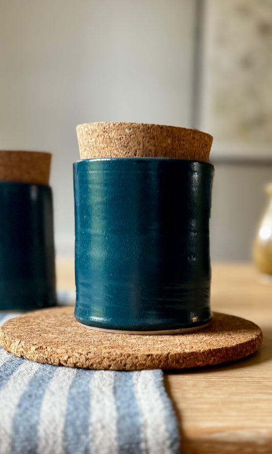 Blue ceramic container with cork lid on a cork coaster on a wooden surface.