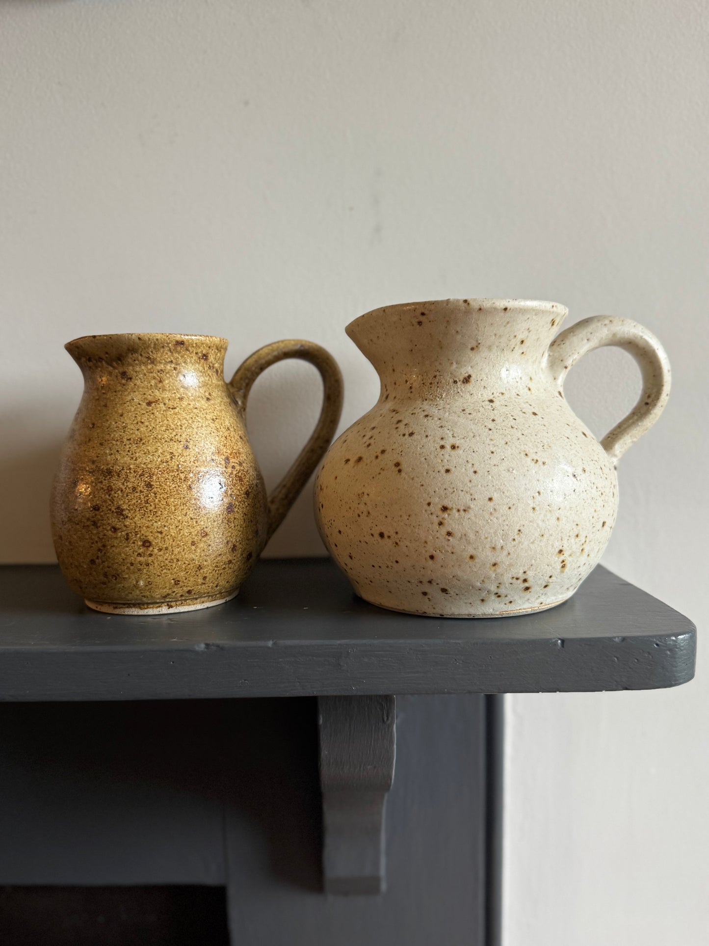 Two ceramic jugs on a dark surface with a neutral background