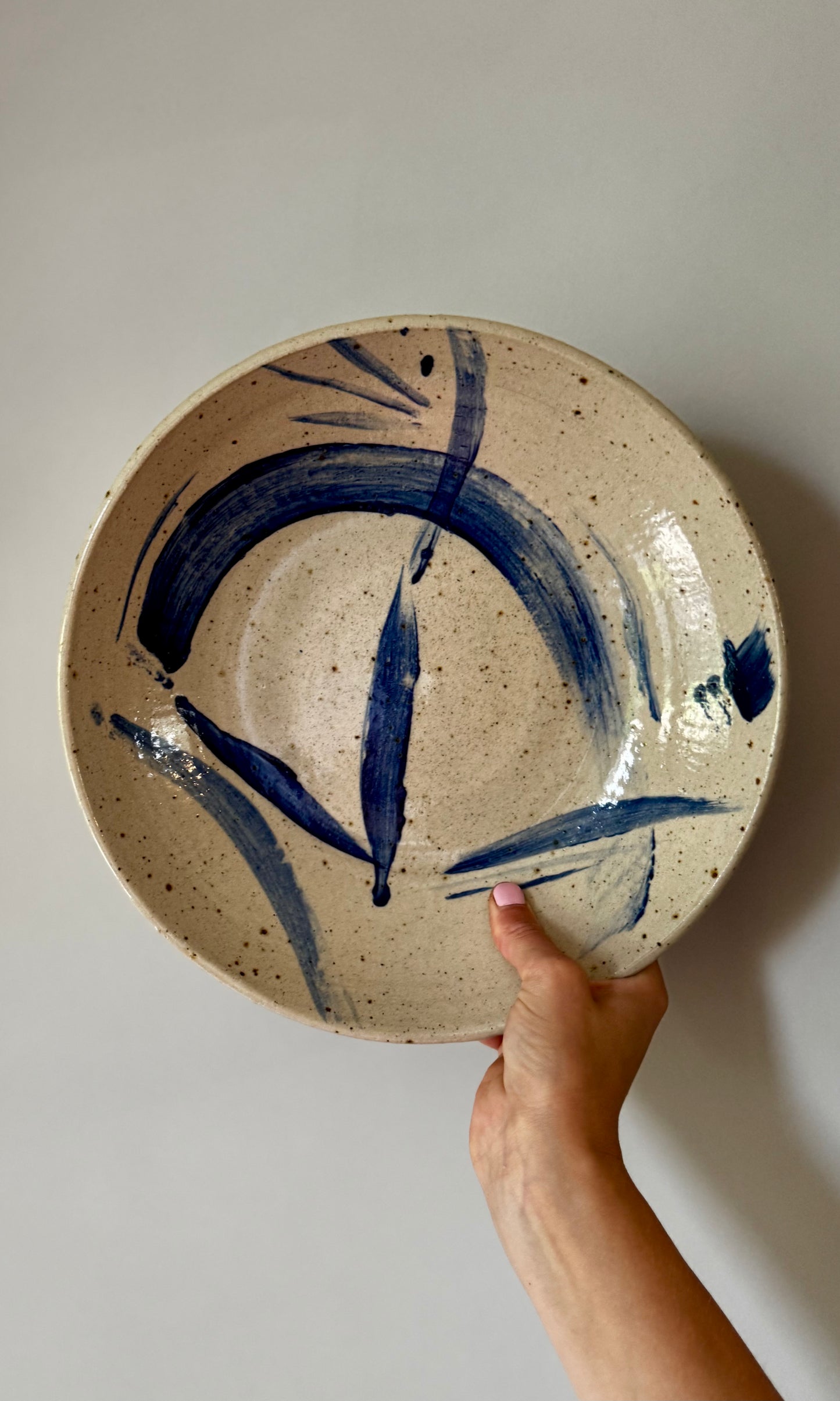 Ceramic plate with blue swoosh design held by a hand against a plain background