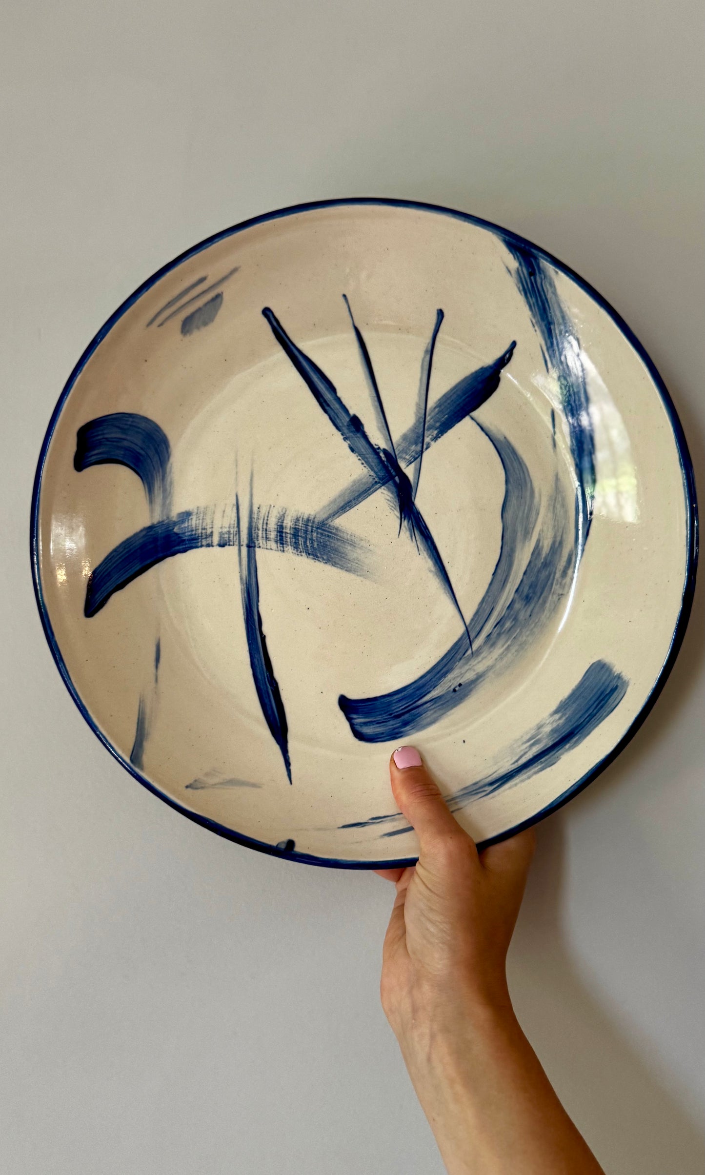 Ceramic plate with blue abstract design held by a hand against a plain background