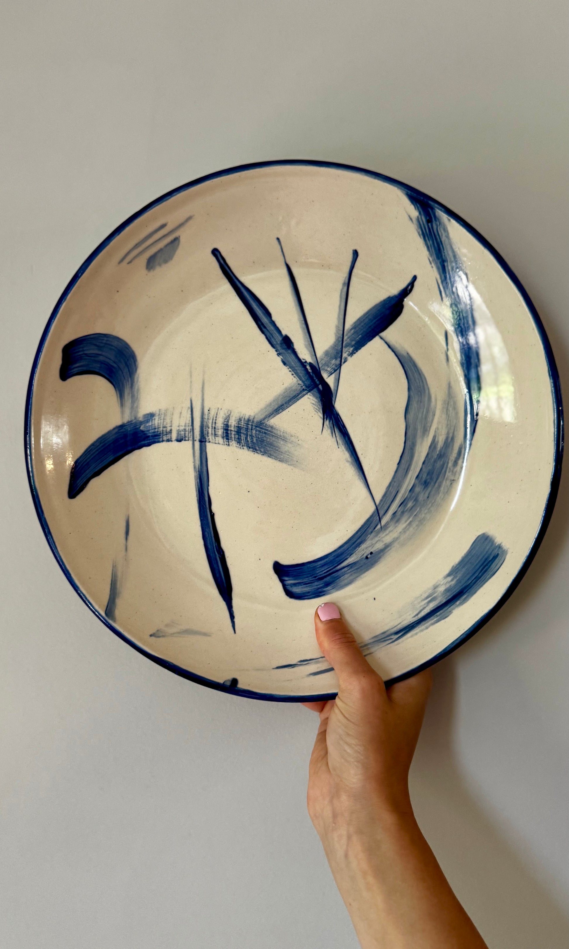 Ceramic plate with blue abstract design held by a hand against a plain background