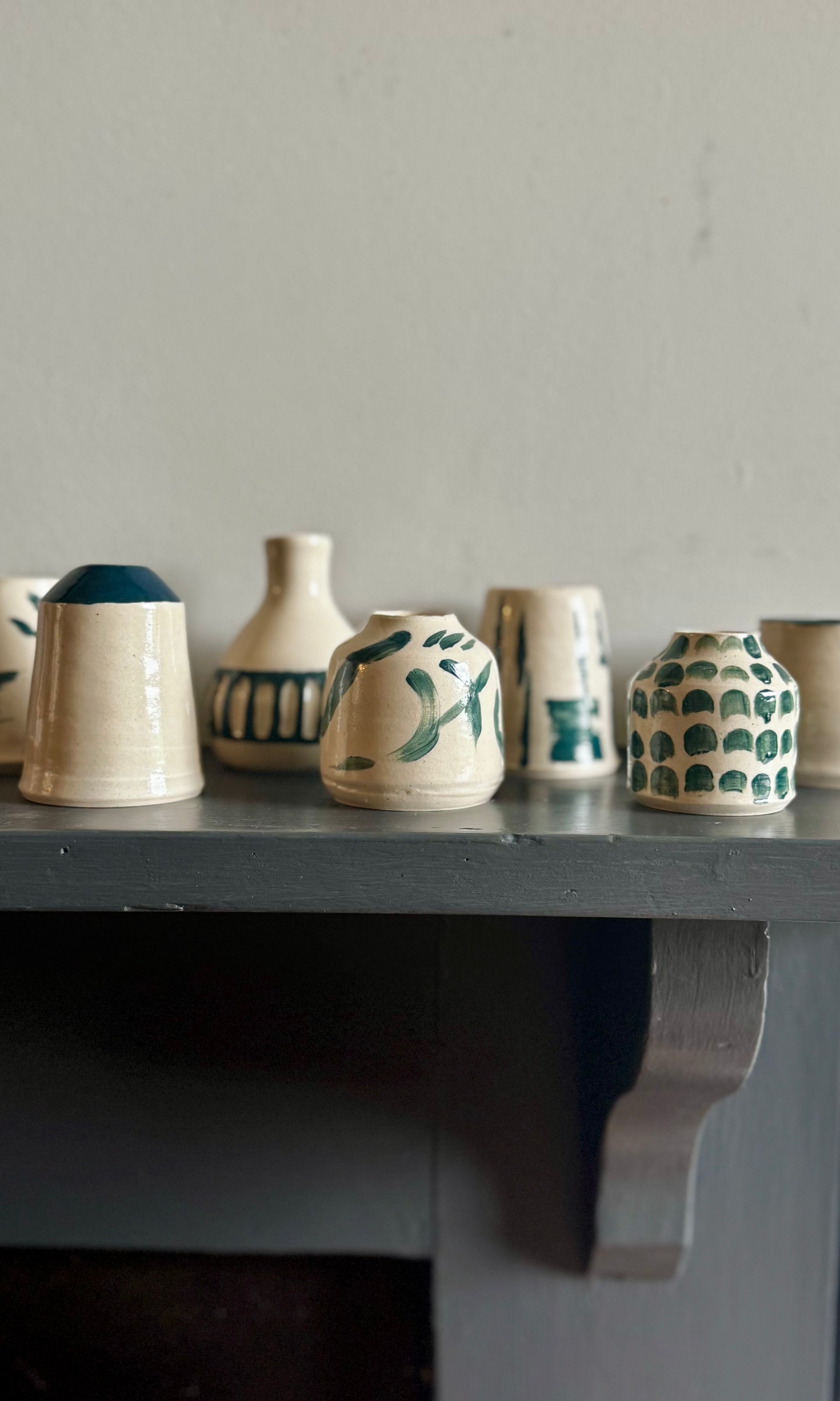 Row of ceramic pots with green patterns on a shelf against a gray wall