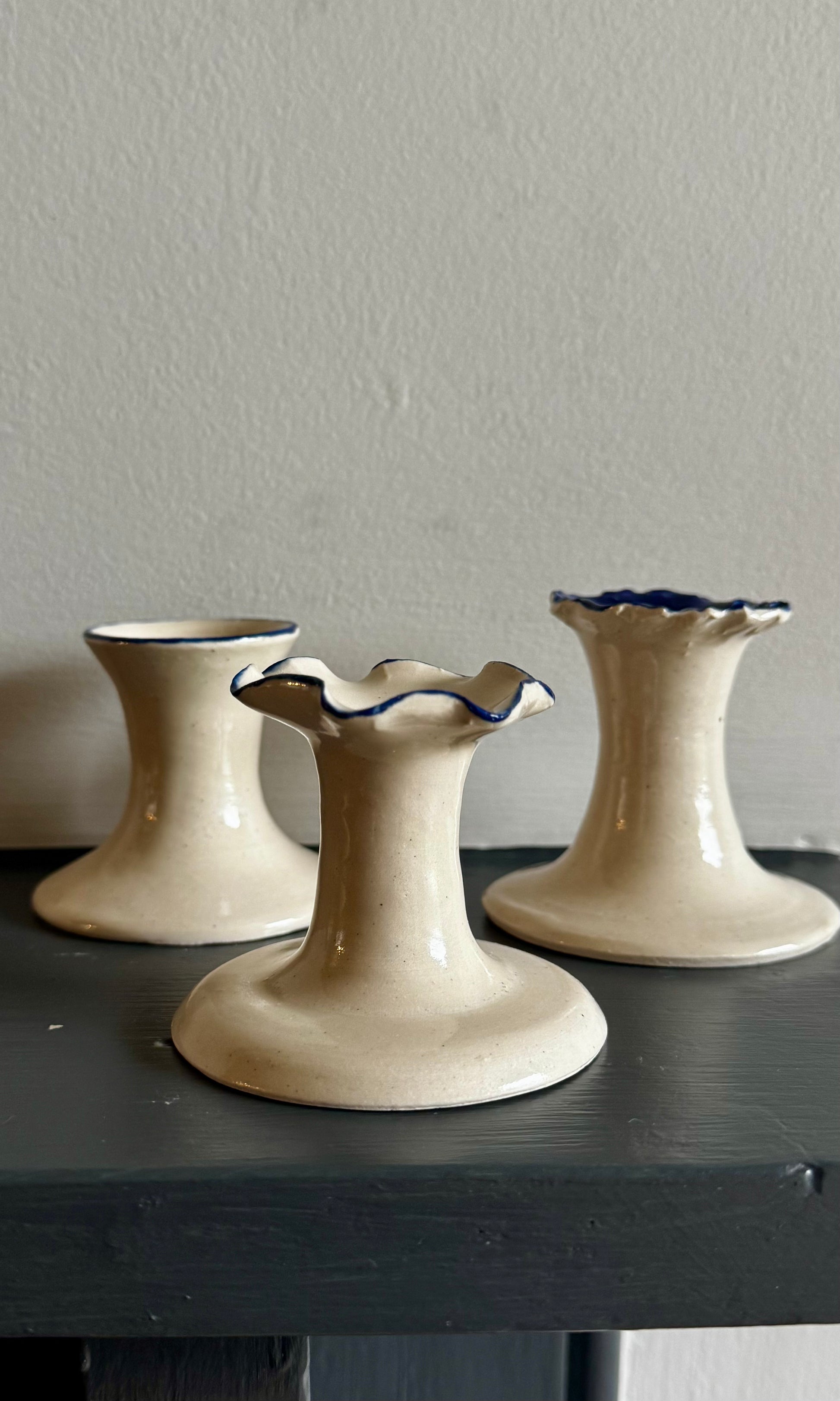 Three cobalt blue ceramic candle holders with ruffled tops on a dark surface against a plain wall.
